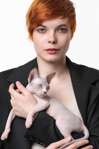 Serious young woman in black jacket holding in hands Sphynx Cat Pretty redhead woman 25 years old