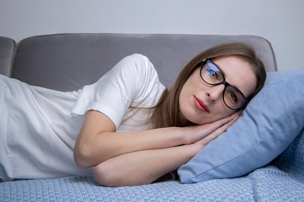 Фото Серьезная молодая женщина в белой футболке с очками лежит на диване