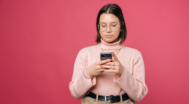 Serious young woman is texting on the phone over pink background