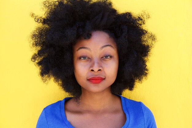 Serious young woman standing by yellow wall staring