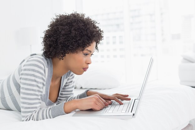 Serious young woman using laptop in bed