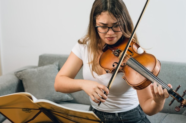 Serious young woman very concentrated practicing the violin at home sitting on the sofa