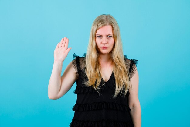 Seriously blonde girl is looking at camera by raising up her handful on blue background