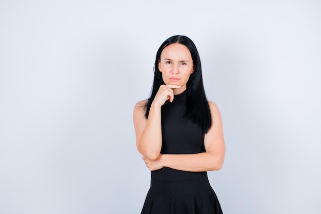 Seriously girl is looking at camera by holding hand under chin on white background