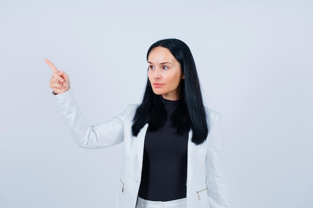 Seriously girl is looking left and pointing there with forefinger on white background