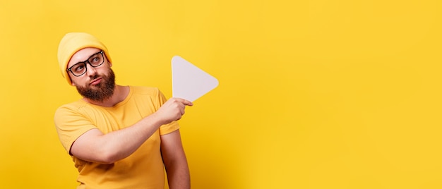 Seriously man holding play button sign over yellow background, technology, media player button, panoramic layout