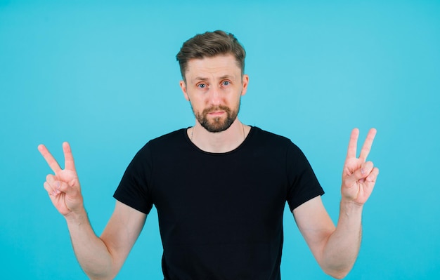 Seriously man is looking at camera by showing two gestures on blue background