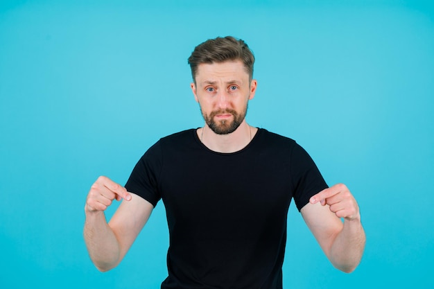 Seriously man is pointing down with forefingers on blue background