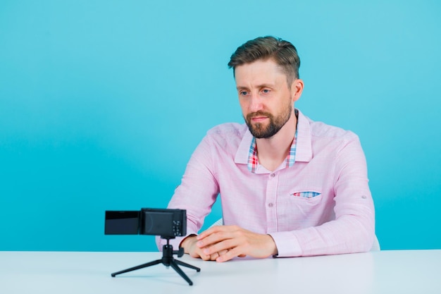 Seriously man is sitting in front of his mini camera on blue background