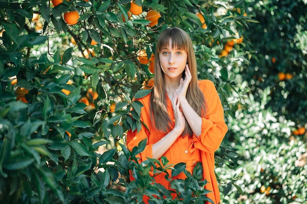 Seriously young girl in orange dress is posing to camera by holding hands up in orange garden