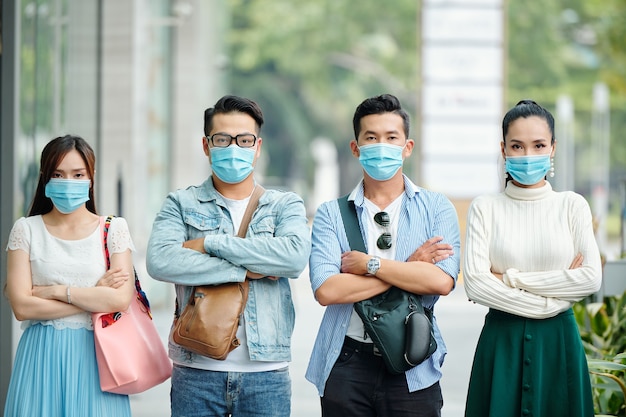 Seroud ongelukkige jonge Aziatische mensen met medische maskers die buiten staan met gevouwen armen