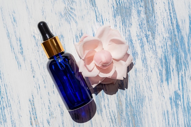 Serum or cosmetic liquid oil on a wooden blue background with rose flower Concept for natural cosmetics not tested on animals Natural ingredients