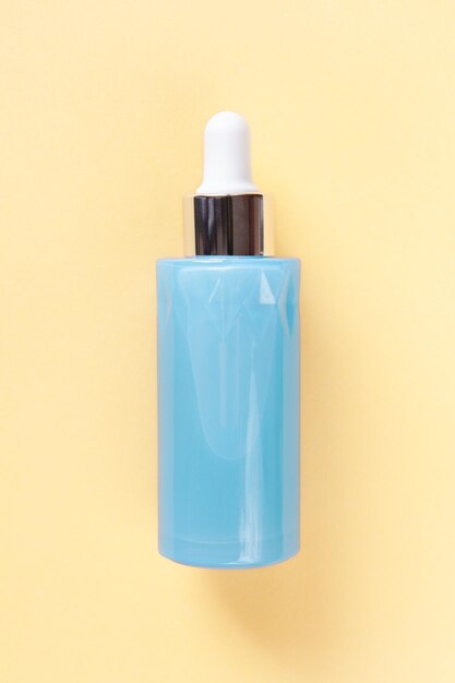 Photo serum for face or eye skin in beautiful blue bottle with dropper on yellow background