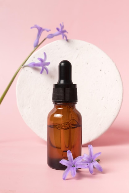 Serum glass bottle with pipette and beautiful flower on pink background Natural Organic Spa Cosmetic concept Front view