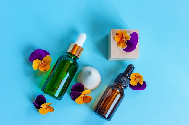 Serum glass bottles with pipette and beautiful viola flowers on blue background. Natural Organic Spa Cosmetic concept. Top view.