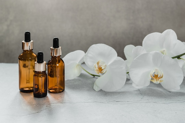 Serum- of etherische olieflesmodel met orchideebloemen op de achtergrond, cosmetische huidproducten voor natuurlijke schoonheid, thuisspa in een druppelflesje