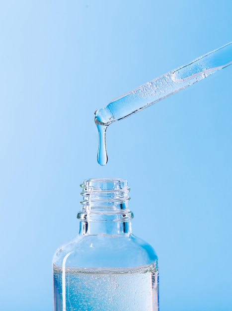 Serum pipette closeup with falling drop on blue background
