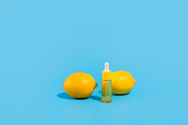 Serum in a transparent bottle with pipette with yellow lemons blue background Cosmetic moisturizer