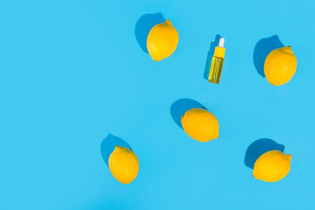 Serum in a transparent bottle with a pipette with yellow lemons on blue background