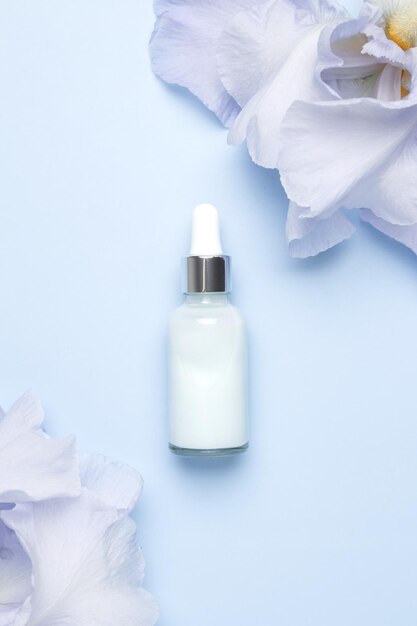 Serum with floral extracts for skincare Nature cosmetics in glass bottle with pipette and iris flowers on blue background Face and body care spa concept