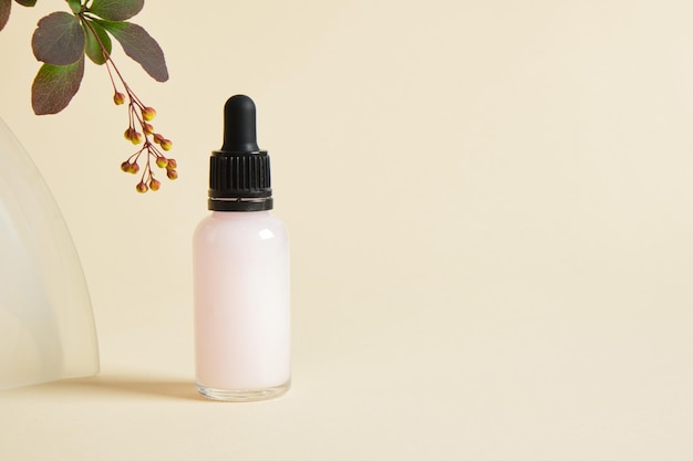 Serums in a transparent dropper bottle and a branch with green leaves and flower buds on a beige background
