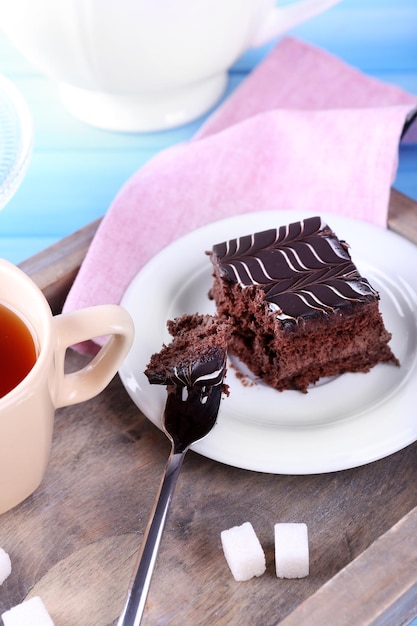 木製の背景のクローズ アップに紅茶とチョコレート ケーキのカップとテーブルを提供しています