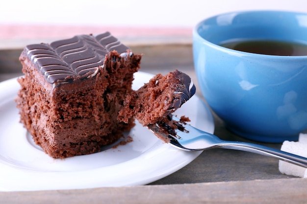 Served table with a cup of tea and chocolate cake on wooden background closeup