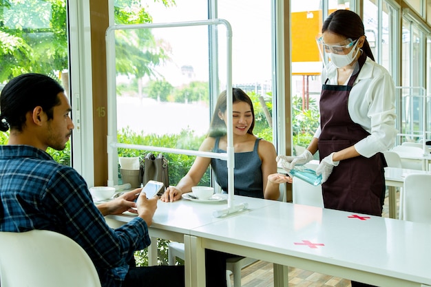 Serveerster die alcoholspray gebruikt voor hygiënische klanthand voordat ze apparatuur aanraakt of luncht in restaurant