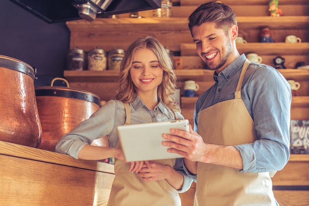 Serveerster en jonge ober in schorten gebruiken een tablet.