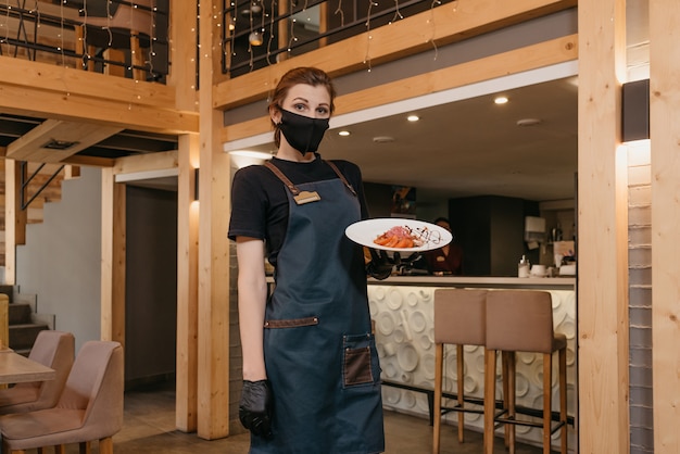 Serveerster in zwarte medische wegwerphandschoenen draagt een medisch gezichtsmasker