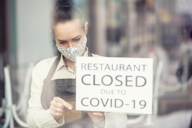 Serveerster plakt bordje met de tekst restaurant gesloten vanwege covid19 op een raam