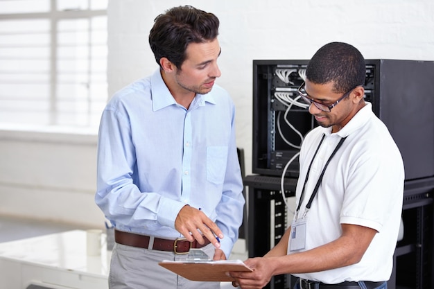 Server room clipboard and discussion with a technician talking to a business man about a cyber security contract Network database and documents with a male engineer chatting about an agreement