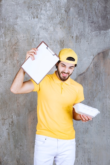 Foto agente di servizio in uniforme gialla che tiene in mano una scatola di plastica per alimenti da asporto e chiede una firma.