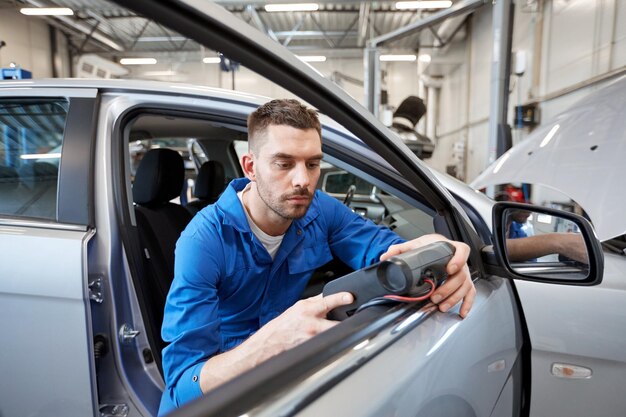 service, repair, maintenance and people concept - mechanic man with automotive diagnostic scanner checking car system at workshop