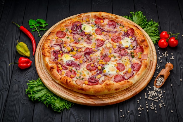 Serving delicious pizza with quail eggs ham sausage and vegetables on a black background