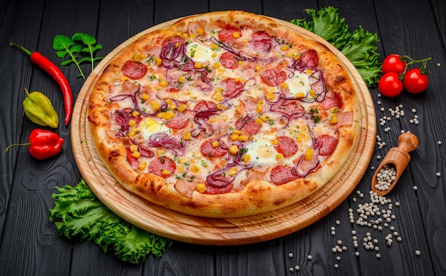 Serving delicious pizza with quail eggs ham sausage and vegetables on a black background