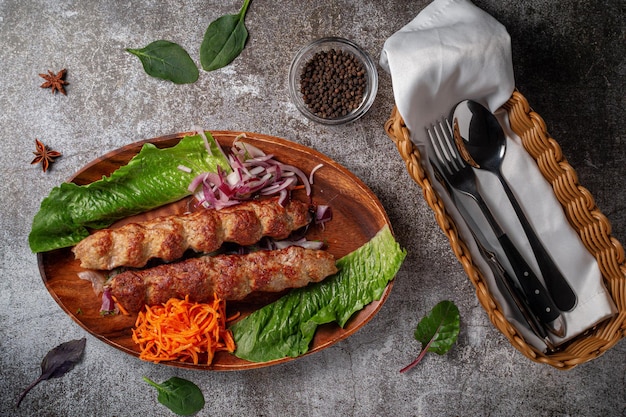 Подача блюда из меню ресторана. Жареная говядина и свинина с тертой морковью и зеленью на тарелке на фоне серого каменного стола, вкусный шашлык