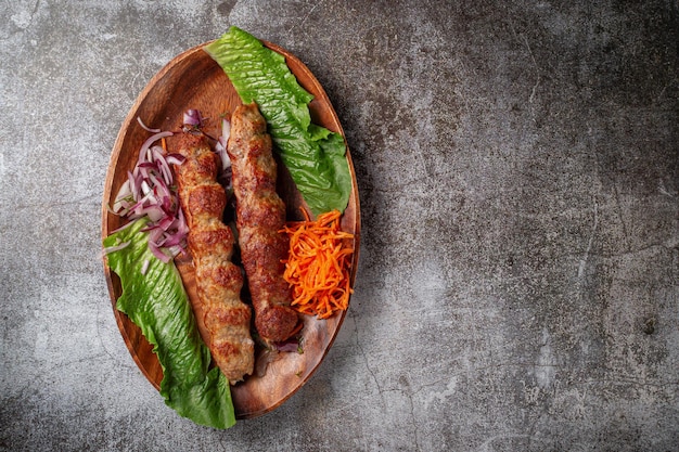 Serving a dish from the restaurant menu. Grilled beef and pork meat with grated carrots and herbs on a plate against a gray stone table, delicious kebab