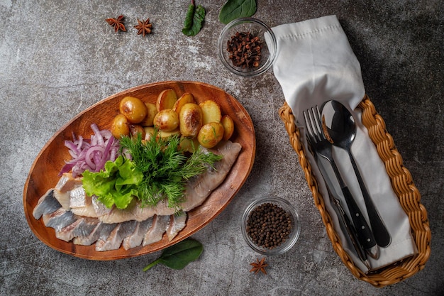 serving a dish from a restaurant menu. salted sliced herring fish with pickled mushrooms and onions, cream sauce, dill and parsley greens on a plate against the background of a gray stone table