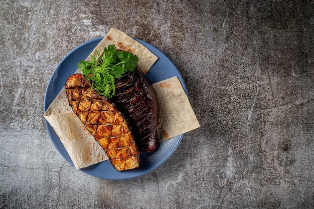 Serving a dish from the restaurant menu. Whole grilled eggplants with herbs on a plate against a gray stone table