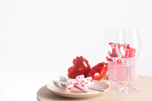 Фото Сервировка для романтического ужина в день святого валентина - столовые приборы и бокалы с тарелкой и красные воздушные шары в форме сердца на столе с копией пространства