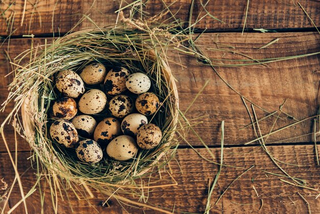 新鮮な卵を提供しています。木製の素朴なテーブルの上の干し草とボウルに横たわっているウズラの卵の上面図
