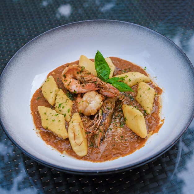 Serving of gnocchi pasta with red curry sauce and shrimps in\
thailand