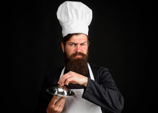 サービングとプレゼンテーションの料理人は、金属製の料理の職業と人々の概念の男性シェフを保持しています
