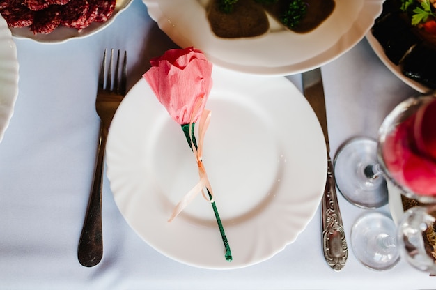 Сервировка, сервировка стола. Одна тарелка столовых приборов и столовые приборы льняная салфетка украшены лентами и цветком.
