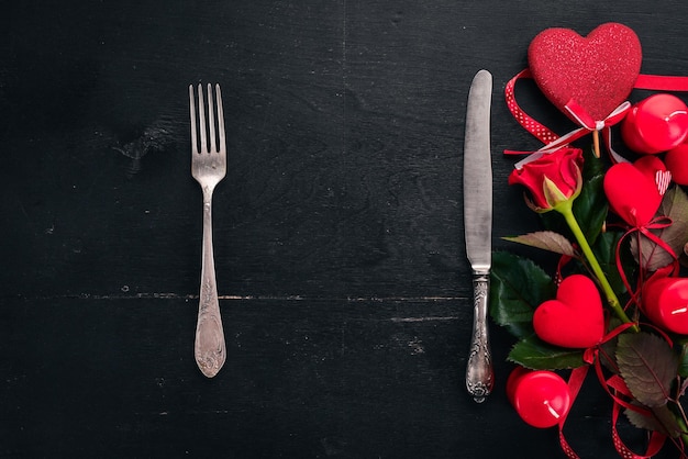 발렌타인 데이를 축하하기 위해 테이블을 제공합니다. 칼 붙이, 접시, 장미. 나무 배경에. 평면도. 텍스트를 위한 여유 공간입니다.