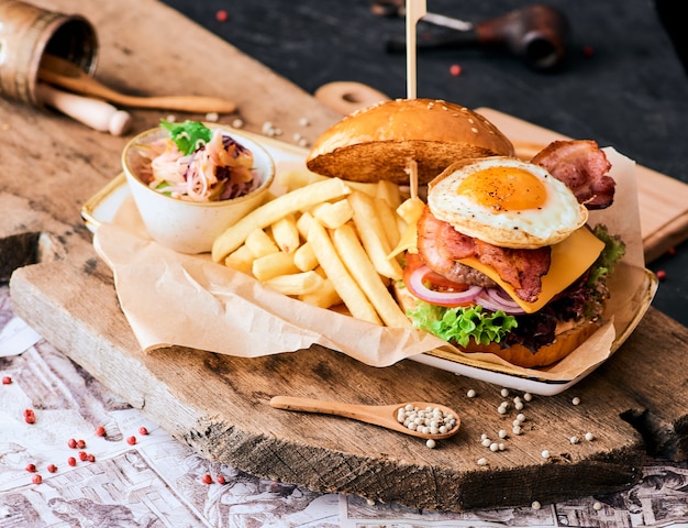 木製のまな板にベーコン、卵、フライドポテトとゴマバーガー。