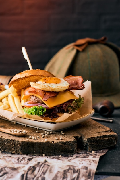 Sesame burger with bacon, egg and french fries on a wooden cutting board.