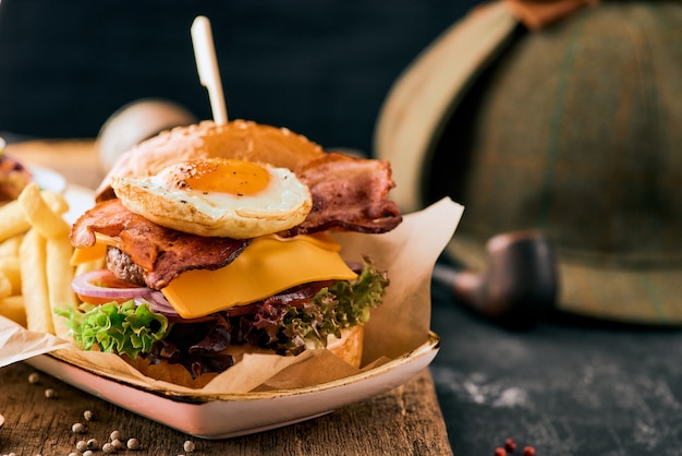 Sesame burger with bacon, egg and french fries on a wooden cutting board.