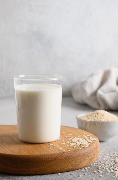 Sesame milk in glass and white sesame seeds in bowl on light background Vegan plant based milk replacer Vertical orientation Close up